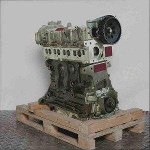 Motor 940 C1.000 auf Holzpalette vor weißem Hintergrund. Der Metallmotor, leicht schräg von oben aufgenommen, zeigt Zahnräder und Zylinderköpfe. Freigestellt.