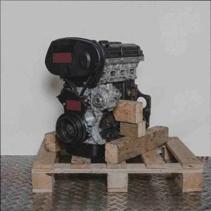 Motor A 18 XER auf Holzpalette vor weißem Hintergrund. Der Zahnriemen und die Riemenscheiben sind deutlich sichtbar. Seitenansicht.