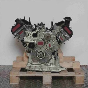 CRTF Motor auf Holzpalette vor weißem Hintergrund. Der V-förmige Motor mit grauen und schwarzen Komponenten ist vertikal ausgerichtet.