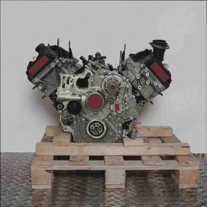 V-förmiger Motor CZVB auf Holzpalette vor weißem Hintergrund. Der Motor besteht aus silbernen und schwarzen Metallteilen und ist vertikal ausgerichtet.