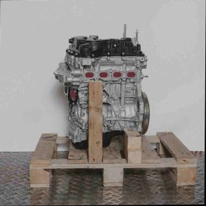 Motor EB2ADTS auf Holzpalette vor weißem Hintergrund. Der silbergraue Motorblock mit schwarzen Abdeckungen zeigt ein schwarzes Bauteil mit weißem Aufkleber. Vertikale Ansicht.