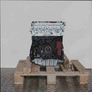Motor F9Q 710 auf Holzpalette vor weißem Hintergrund. Der schwarze Motorblock und silberne Zylinderkopf sind deutlich zu erkennen.