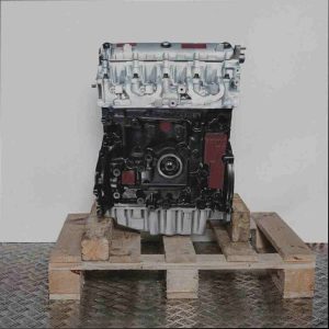 Motor F9Q 716 auf Holzpalette vor weißem Hintergrund. Der schwarze Motorblock und silberne Zylinderkopf sind deutlich zu sehen, ebenso wie Anschlüsse und Ölfilter. Seitliche Ansicht des Motors.