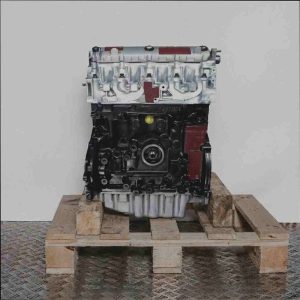 Motor F9Q 717 auf Holzpalette vor weißem Hintergrund. Der schwarze und silberne Motor ist von der Seite zu sehen.