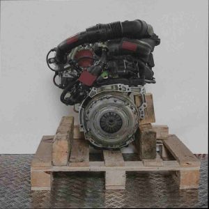 Seitenansicht eines Motors HNP (EB2ADT) auf einer Holzpalette vor weißem Hintergrund. Der Motor zeigt schwarze Schläuche und metallische Komponenten, einschließlich einer Kupplung.